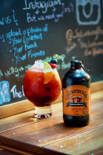 A Berry Sarsaparilla Mocktail on bar with berries & lime for garnish